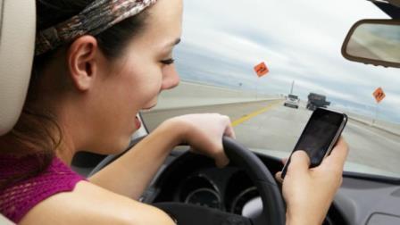 young woman driving on highway while reading / writing text on smart phone.